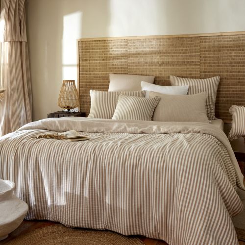 Lit élégant avec housse de couette gaze de coton rayures dans une chambre lumineuse