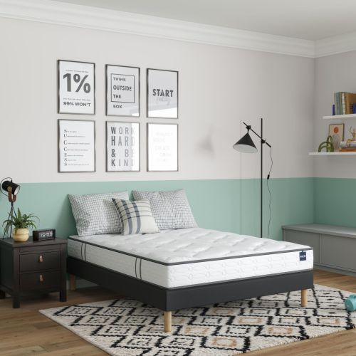 Matelas mousse ferme Bultex Le Surprenant présenté sur un sommier tapissier noir dans une chambre.
