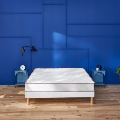 Matelas en ressorts ensachés ferme Merinos Le Chanceux installé sur un lit face à un mur bleu