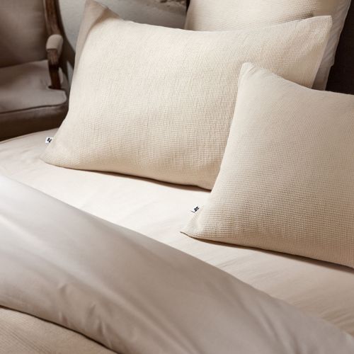 Taie d'oreiller écru Maya en coton déposée sur un lit au design contemporain et épuré