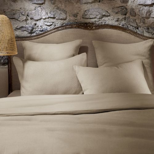 Taie d'oreiller écru Maya en coton déposée sur un lit au design contemporain et épuré