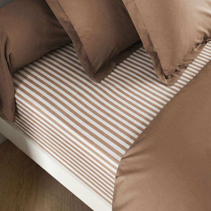 Drap housse en coton rayures marron installé sur un lit dans une chambre chaleureuse