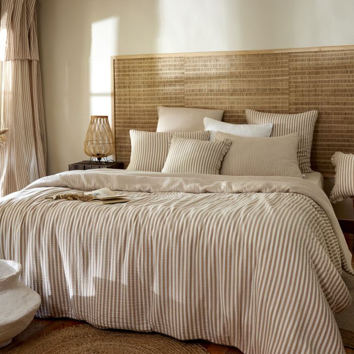 Lit élégant avec housse de couette gaze de coton rayures dans une chambre lumineuse