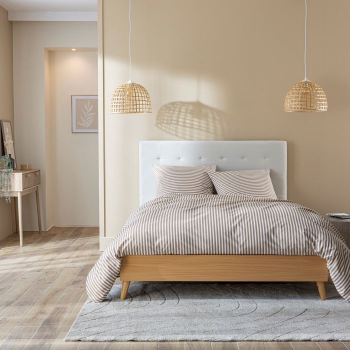 Lit fait avec tête de lit capitonnée en velours écru et structure en bois avec matelas dans un décor de chambre de face ambiance principale