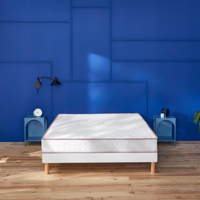 Matelas en ressorts ensachés ferme Merinos Le Chanceux installé sur un lit face à un mur bleu