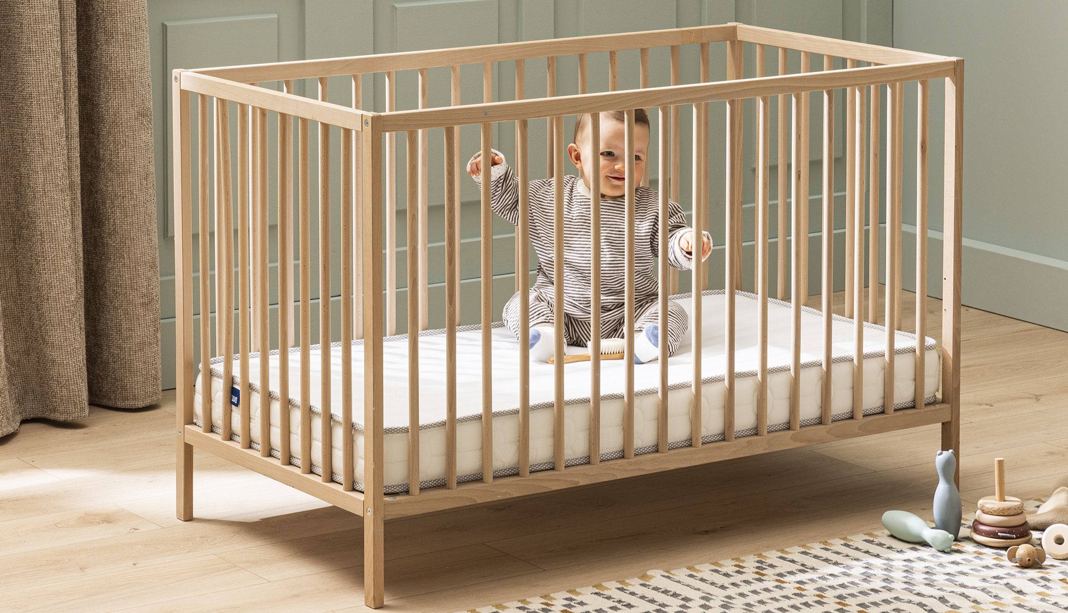 Bébé assis dans son lit en bois sur le matelas bébé en mousse ferme Bultex Pilou.