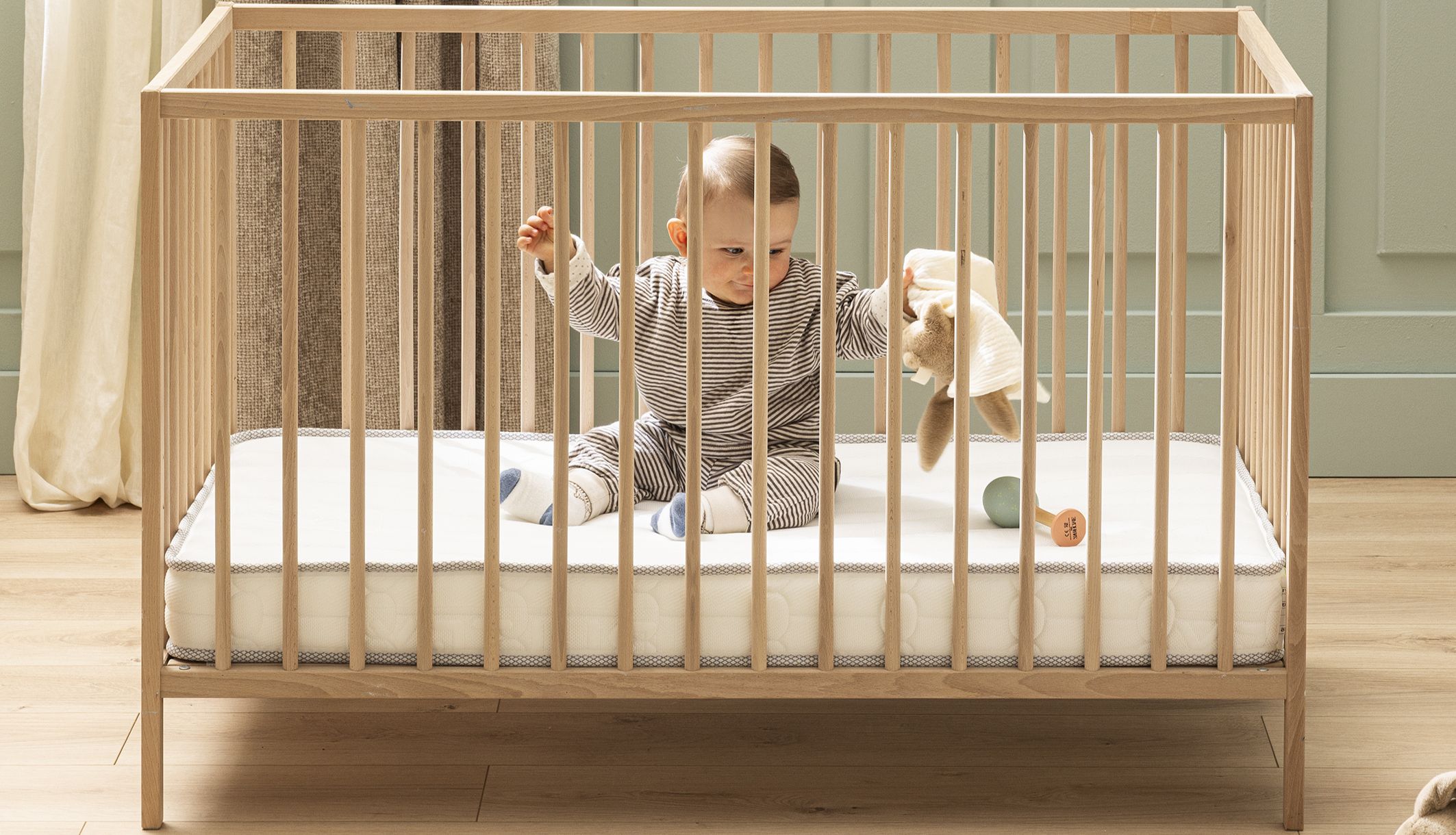 Bébé de face jouant avec son doudou sur un matelas lit bébé Bultex.