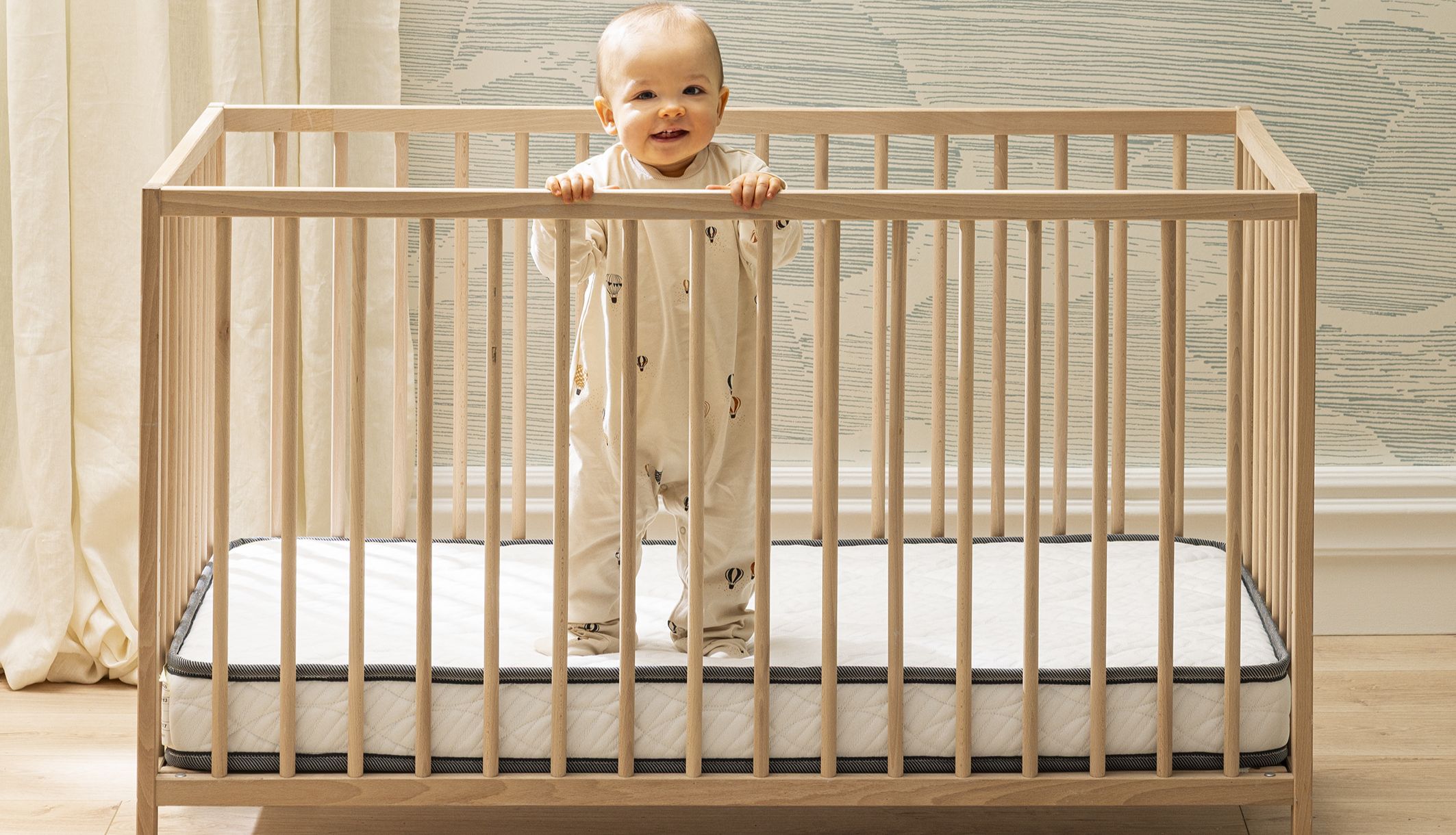 Enfant souriant debout de face dans son lit sur un matelas Bultex bébé.