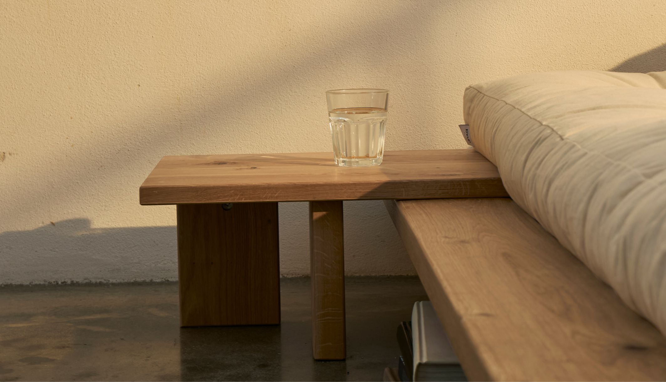 Détail de face d&#039;une table de nuit chêne avec verre d&#039;eau près du matelas.
