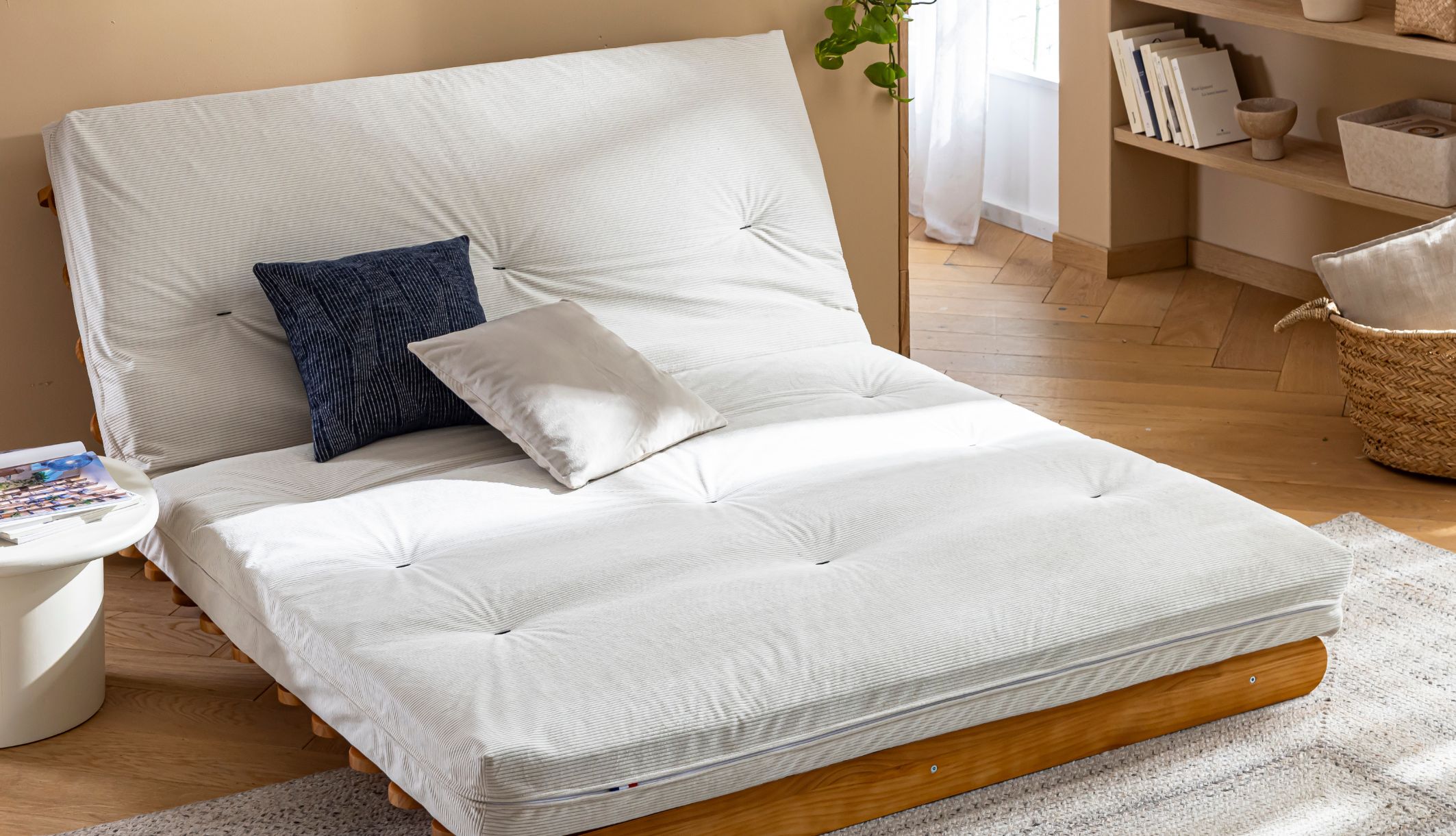 Futon latex de couleur écru déplié sur sa structure en bois avec deux coussins.