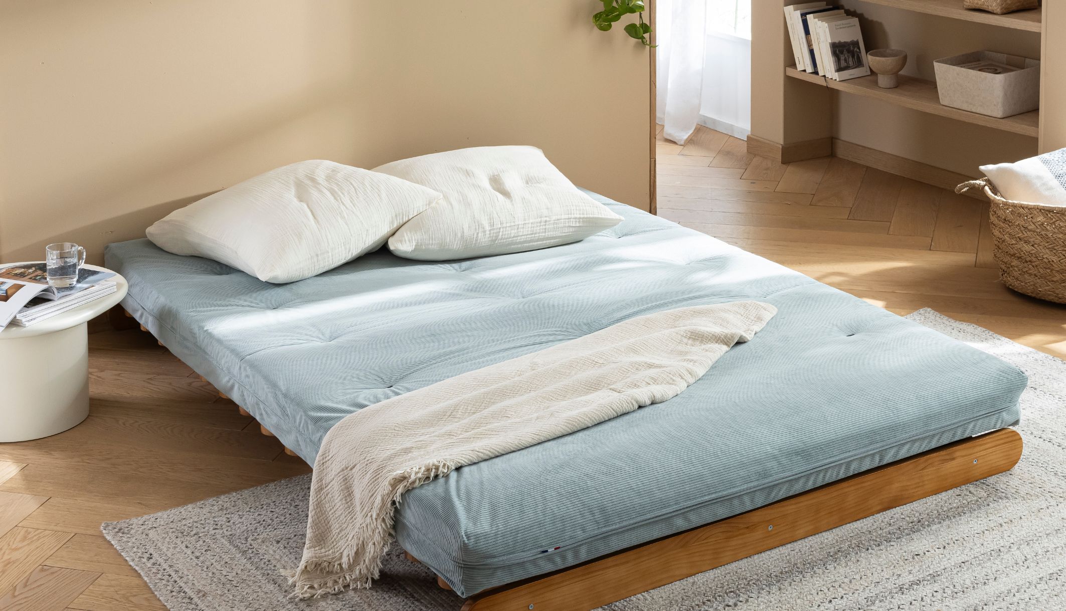 Matelas japonais vert céladon dressé à plat en lit d&#039;appoint avec oreillers et plaid.